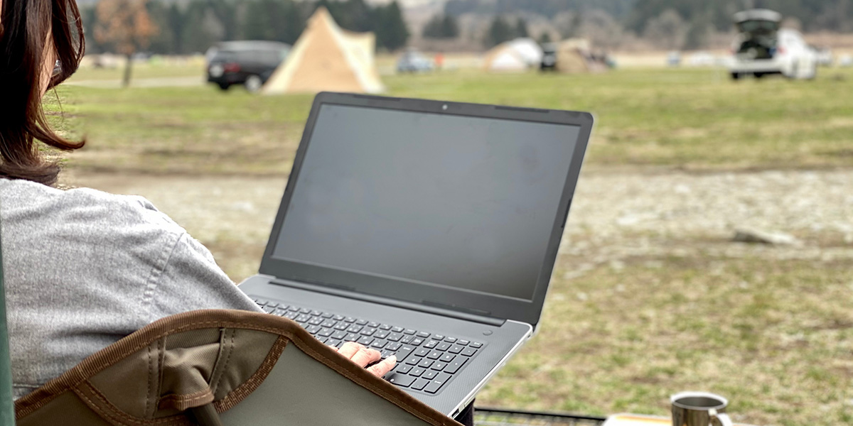 A woman sitting outdoors and using her laptop while she's camping