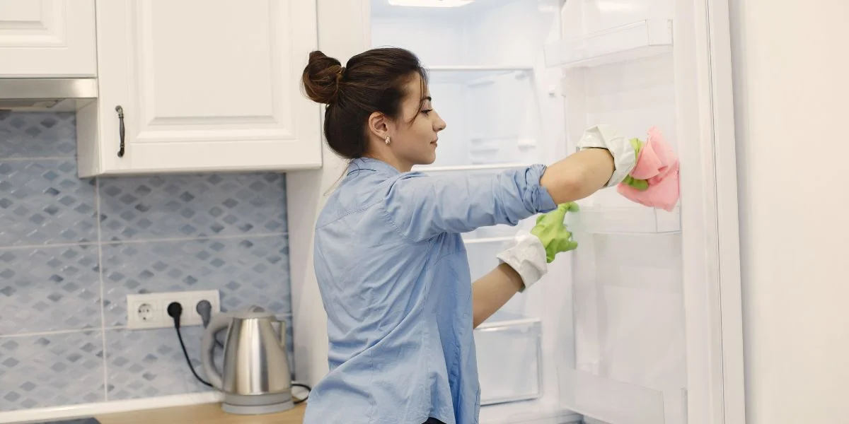 A woman cleaning the door bins of her refrigerator.