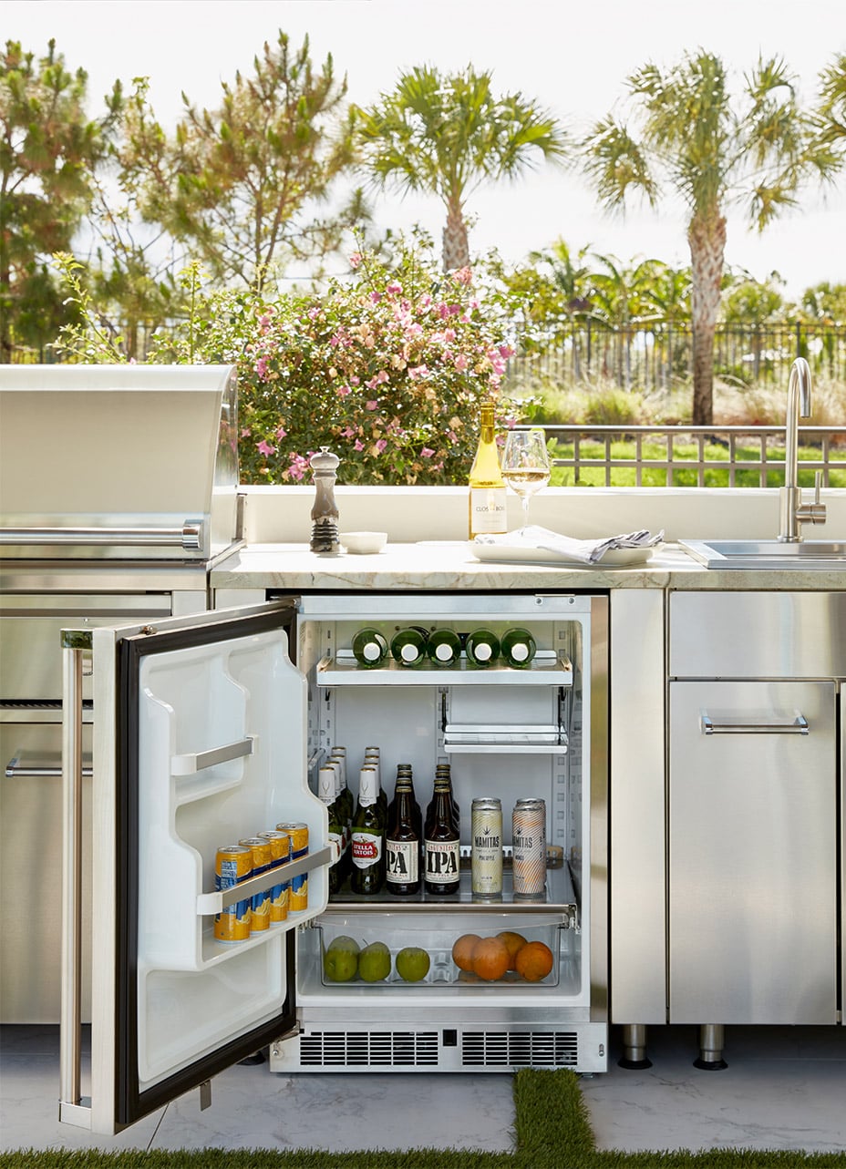 A detailed shot of a built in viking outdoor refrigerator, where the door is open showing what drinks and fruits are inside