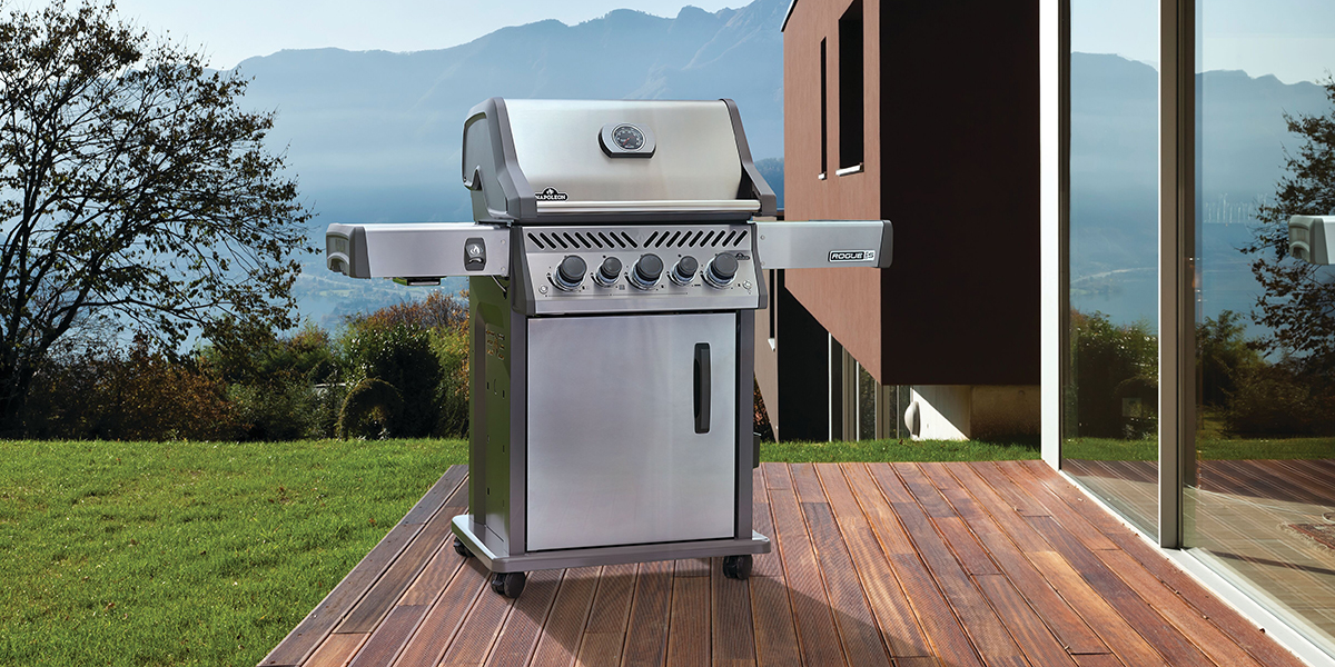 A stainless steel outdoor grill sitting on a wooden patio in front of a mountain range