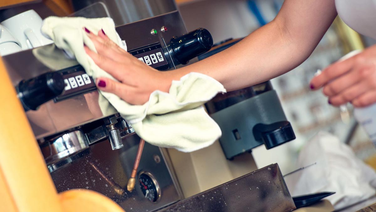 Person wiping down the exterior of a stainless steel espresso machine with a cloth