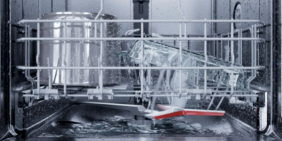 The interior of a dishwasher while it runs, focusing on the spinning arm and spouts of water.