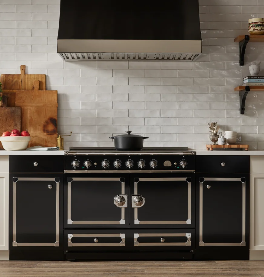 Black La Cornue range in a kitchen with white subway tile, a black hood, and rustic wood cutting boards