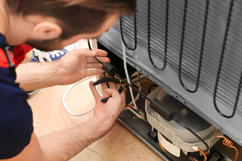 Repair person looking at back of refrigerator