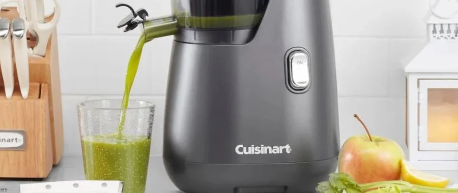 A Cuisinart juicer crafting a green juice from spinach, juice and lemons on a countertop beside ingredients and a knife block.
