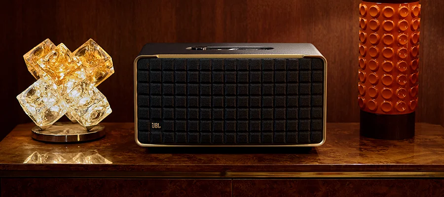 The JBL Authentics 500 speaker sitting on a wooden table between a glass light and an orange lamp