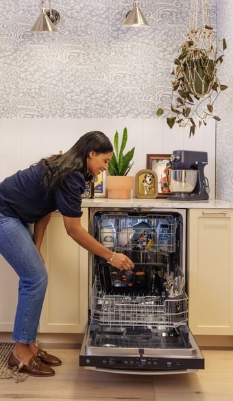 person bending over to unload the open ge profile dishwsher showcasing its size and space