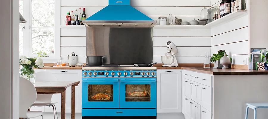 A turquoise blue range and range hood cooking in an all white kitchen