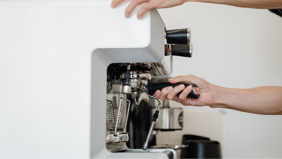 Person pulling the handle on a white espresso machine