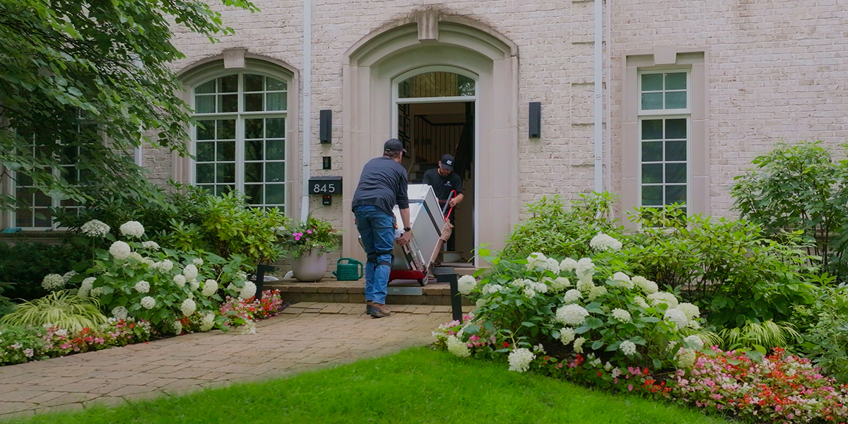 Two Abt delivery drivers/installers wheeling an appliance through the front door of a residential home
