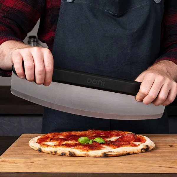 Someone using a pizza cutter rocker blade to cut a pizza on a cutting board