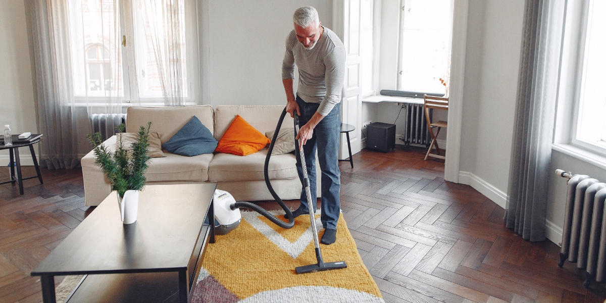 A man using a vacuum to clean an area rug in his living room