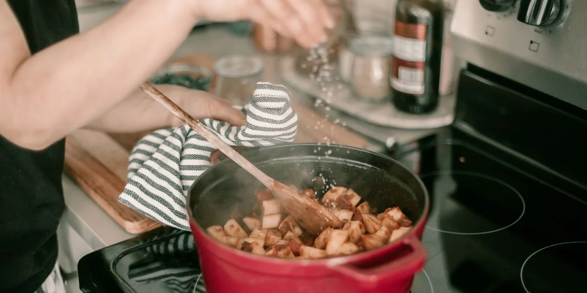 A person cooking potatoes in a red Dutch oven.