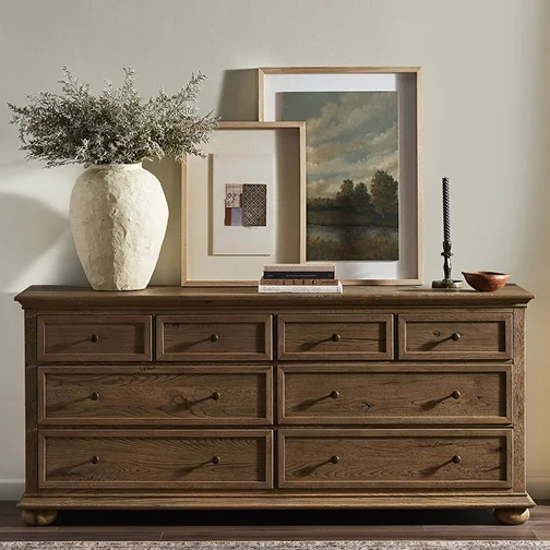 A wooden dresser featuring a decorative vase and a framed picture on top