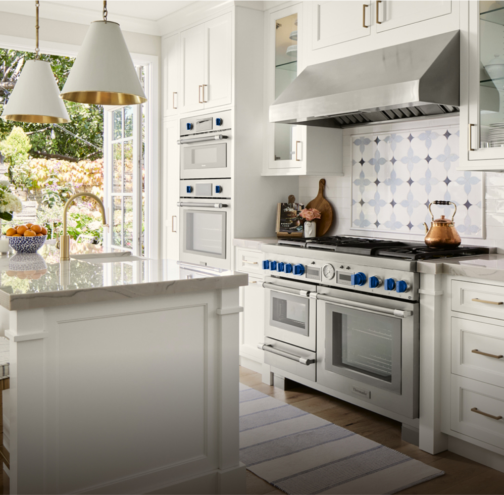 Modern kitchen with white cabinets, blue accents, and high-end Thermador Professional Collection appliances, including a range, rangehood, and wall oven
