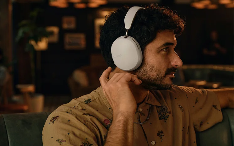 Sonos Ace Headphones atop a head of agentlement looking right showing off the headphones from the side with the sonos logo