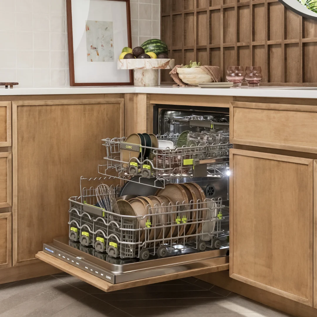 A woman stands in a modern kitchen featuring a built-in cove dishwasher and a Wolf range in the background