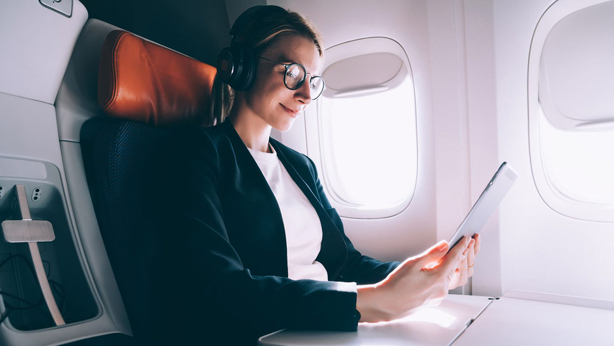 Woman sitting on a plane holding a tablet and wearing headphones