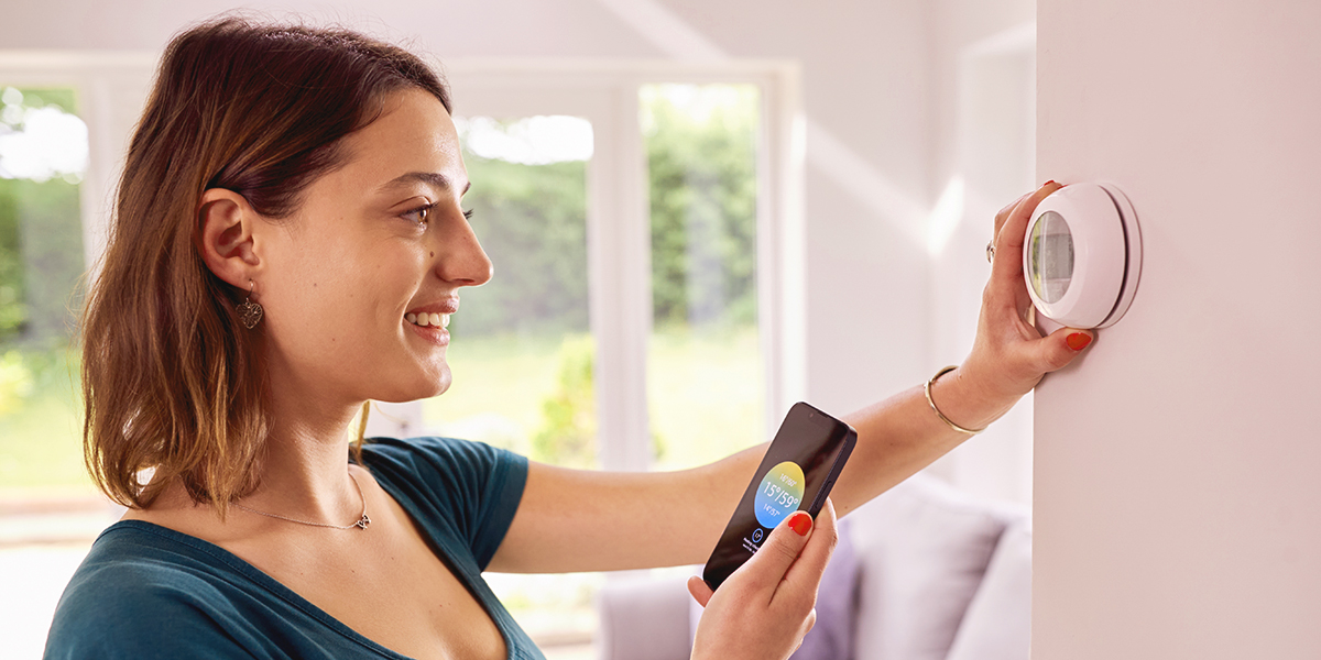Woman adjusting her smart thermostat while holding her smartphone with the thermostat app