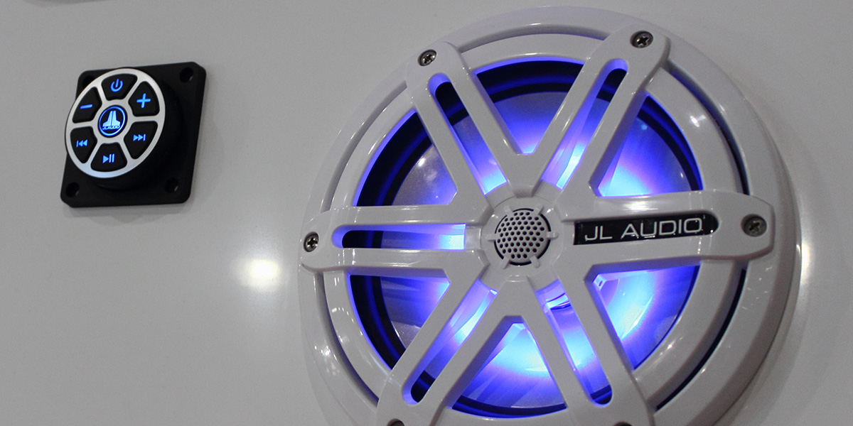 A white boat background with a large white and blue JL audio speaker and touch controls