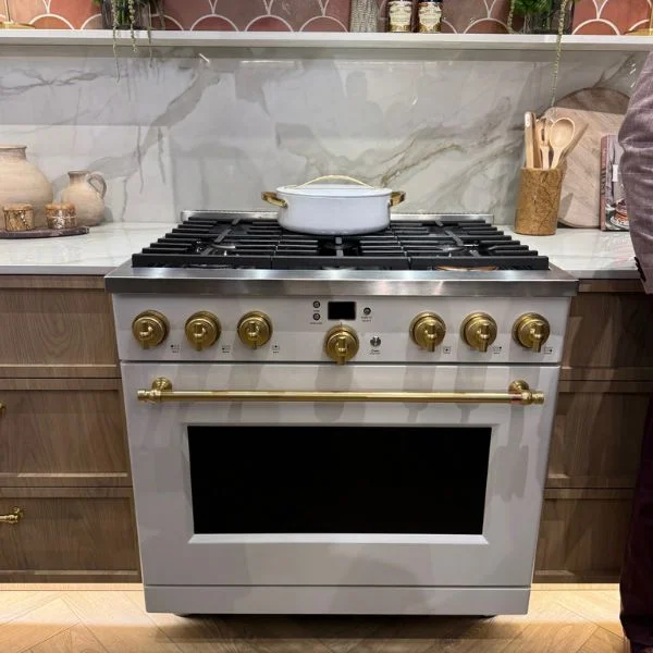 White Cafe range with brass knobs and handle against a marble backsplash