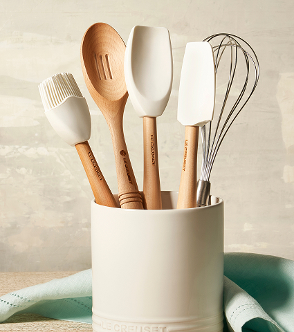 A jar with a basting brush, wooden spoon, spatulas and a whisk