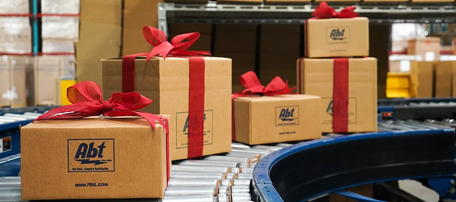 Several Abt labeled boxes wrapped with red bows rolling down an assembly line