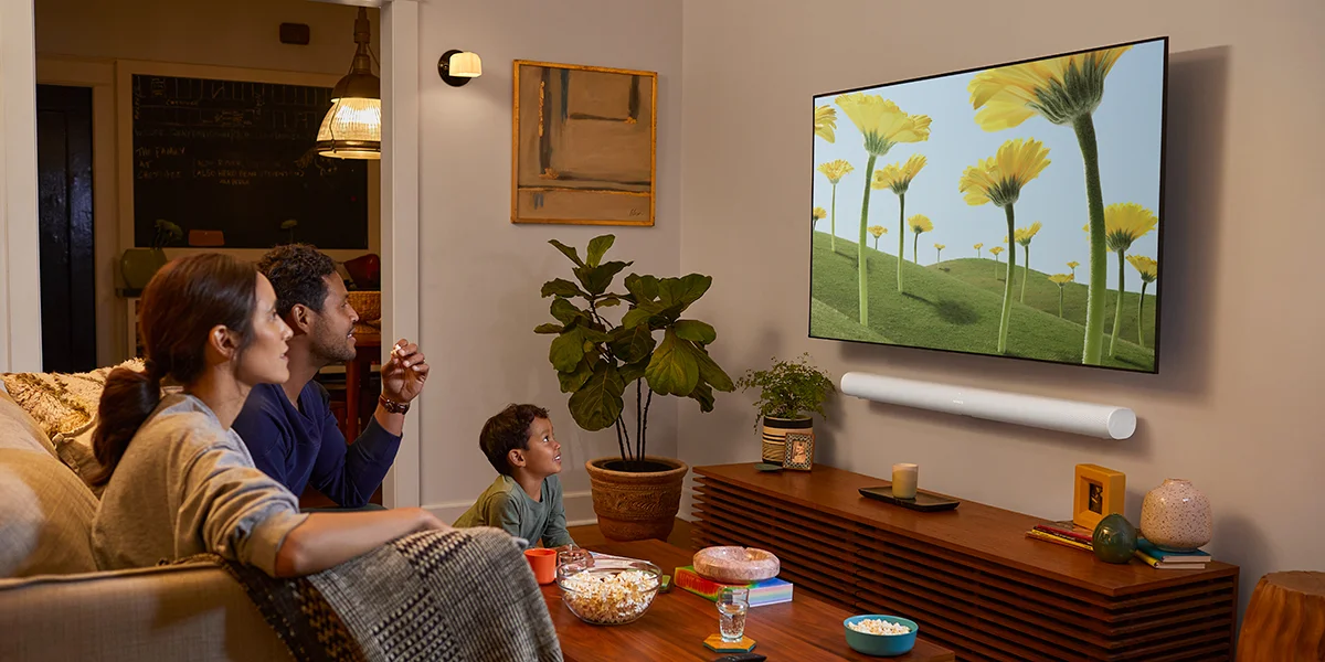 A family sitting in the living room watching TV with a white soundbar mounted beneath it