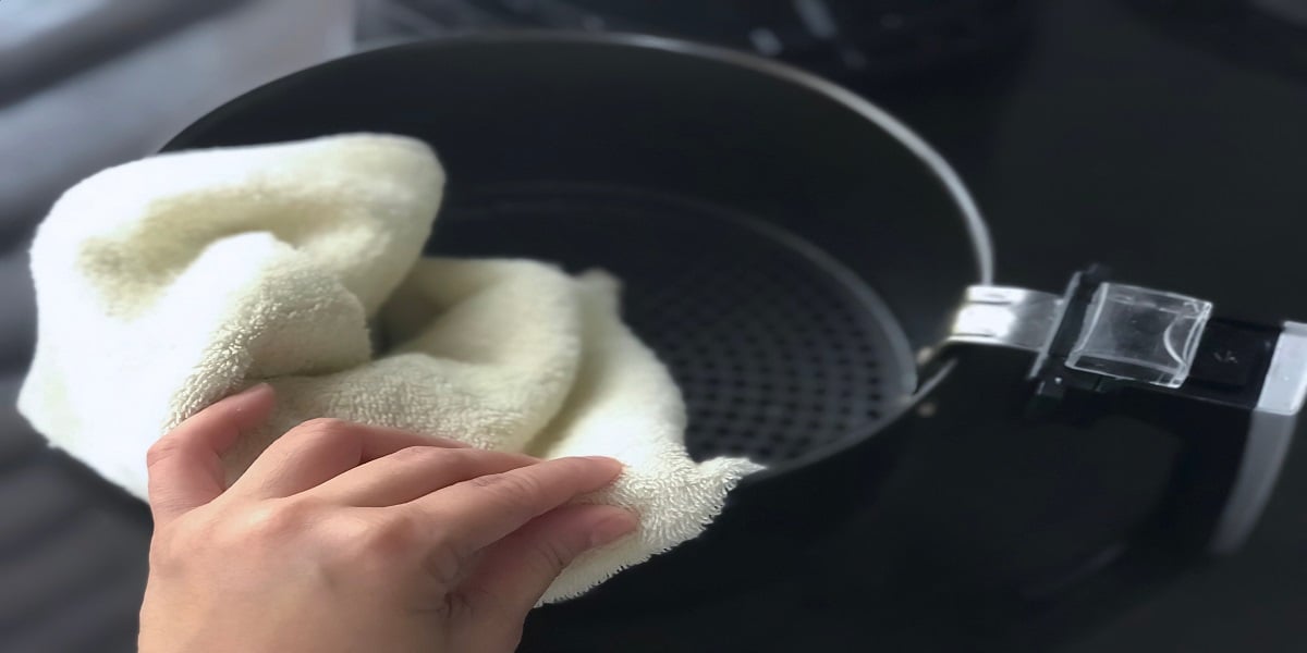 Hand wiping an air fryer basket with white cloth