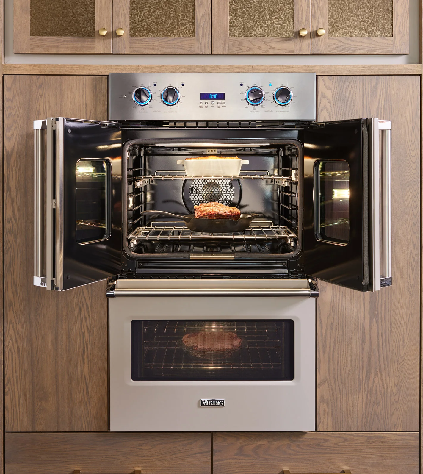 A stylish kitchen equipped with a Viking Double Wall Oven with the top oven doors open showing a roast cooking in a cast iron skillet