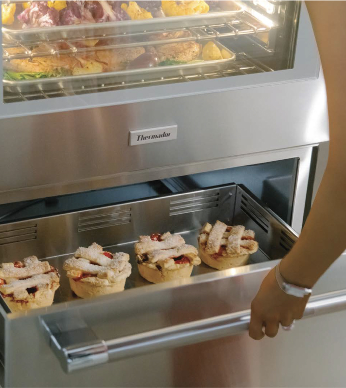 Person removing a pie from a Thermador warming drawer, showcasing the appliance's functionality and design