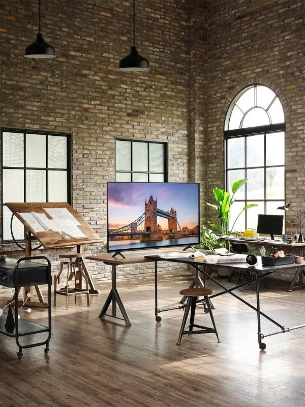 An ultra 4k TV in a modern home with exposed brick, a tv on a wooden topped tale and an easle showcasing a studio like enviornment