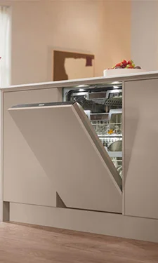 Tight shot of a miele dishwasher built into a kitchen with the door slightly adjar showcasing the stainless steel interior lit up