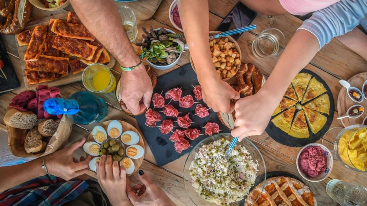 aerial view of table covered in different plates and bowls of food with people serving themselves