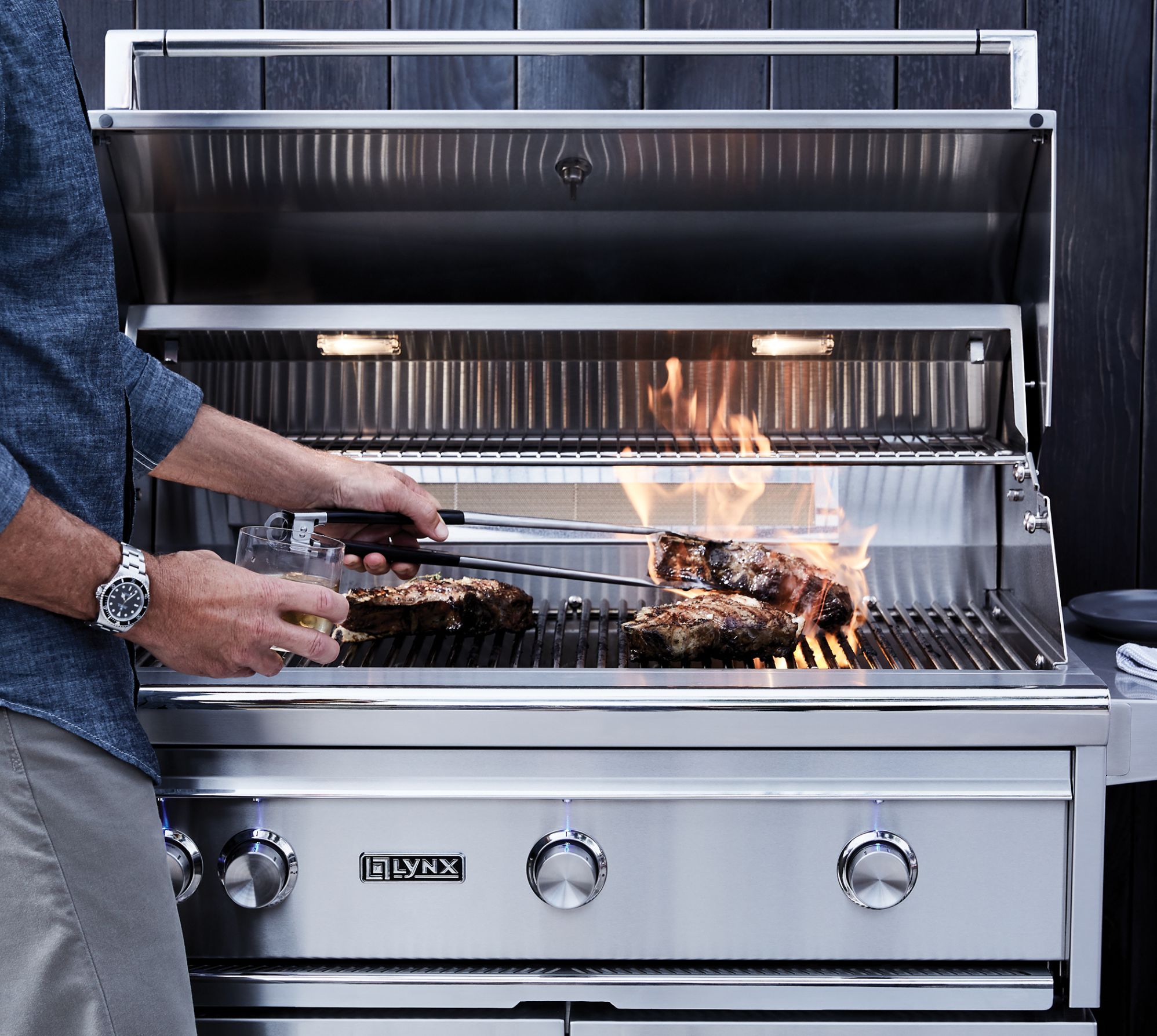 closer-up of a lynx stainless steel grill with bbq meat and sauce off to the side of the grill