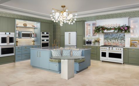 Wide angle shot of a moden kitchen with green cabinets and a blue island with all white stainless appliances from Cafe