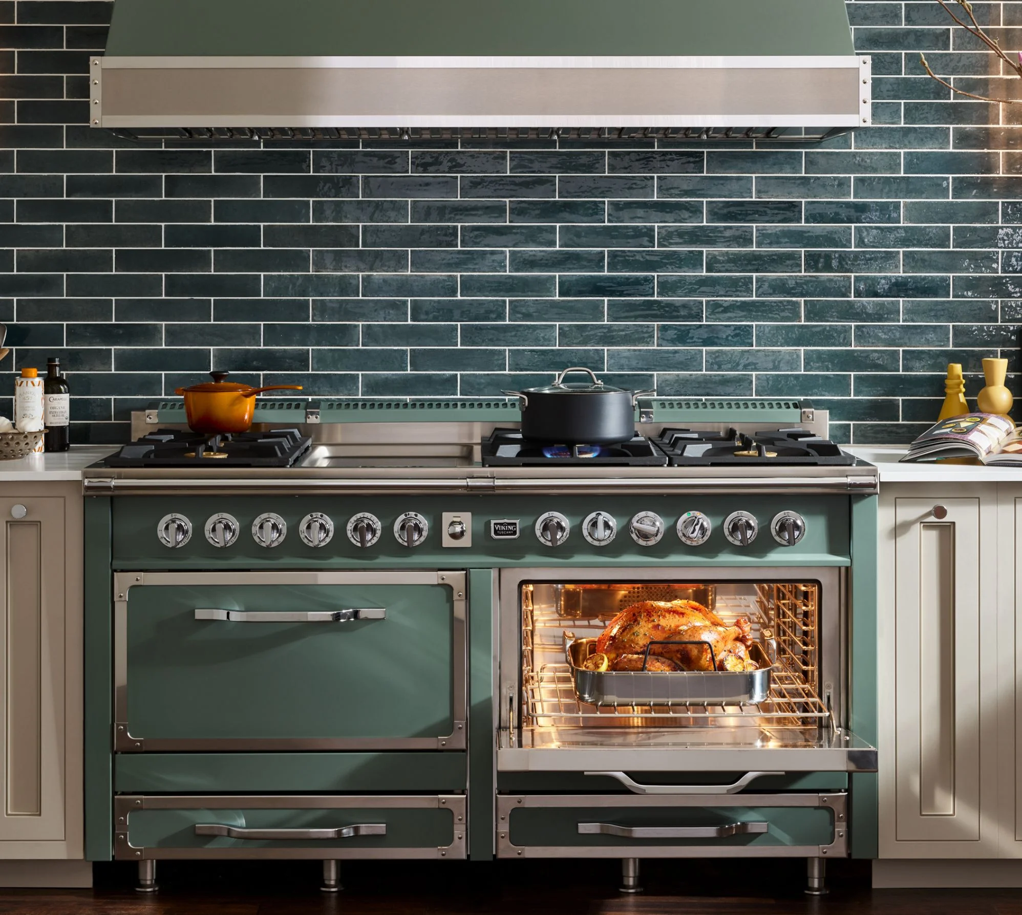 Wide shot of the viking tuscany range in green blue in a modern kitchen setting with green tile backsplash and a chicken in the oven