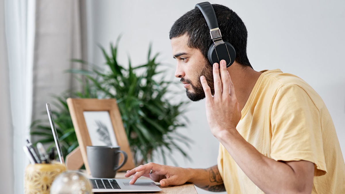 Man in a yellow shirt wearing headphones and using a laptop