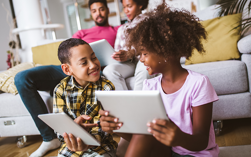 family enjoying time together while the kids play on their tablets and parents browsing on their laptop