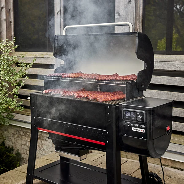 The Weber Searwood 600 XL sitting on a stone patio outside. The lid is open and several rib racks are being grilled.