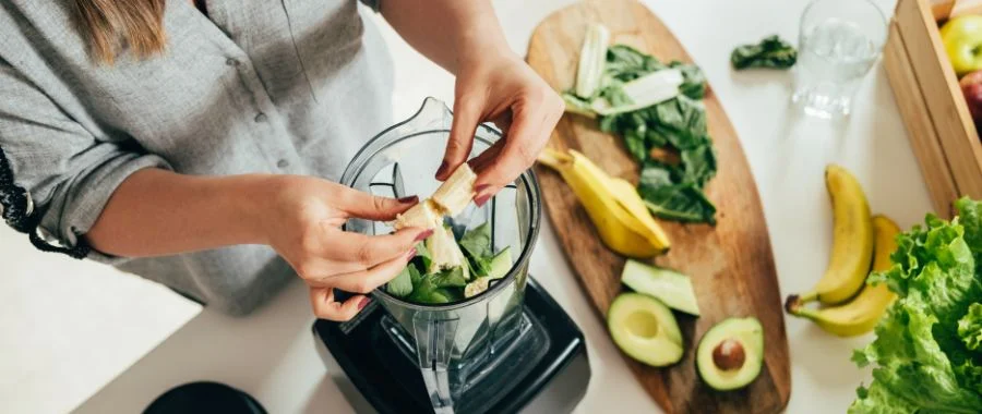 Person making a green smoothie with a blender, greens, avocado, banana and more.