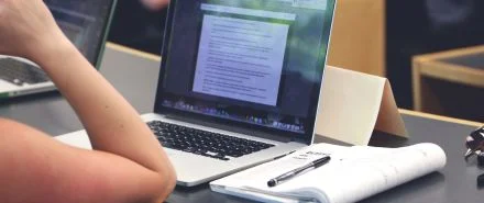 A student reading notes while in class on their laptop.