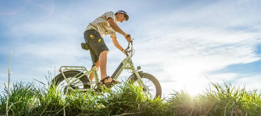 man wearing a baseball hat riding on an electric bike through grass