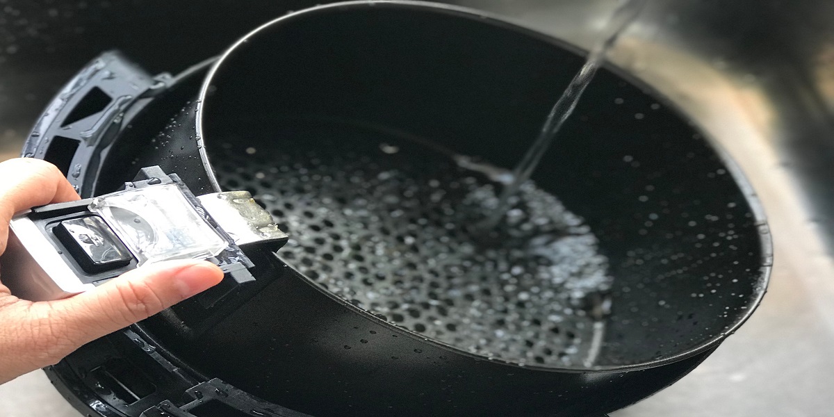 Hand holding air fryer basket under running water