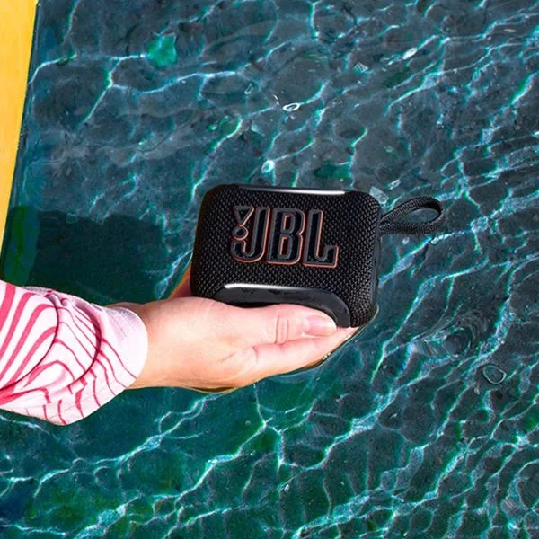 Person holding a black JBL Go 5 speaker above a body of water.