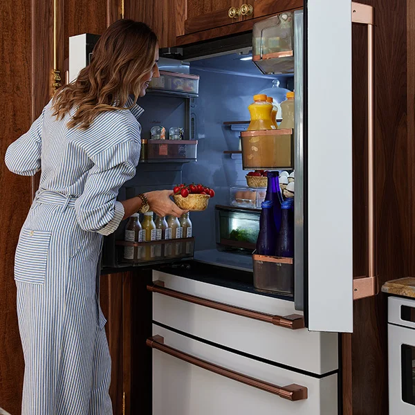 woman wearing striped jumpsuit taking tomatoes out of a matte white fridge