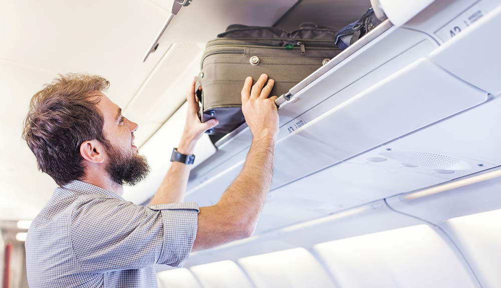 Person placing suitcase in overhead airplane bin.