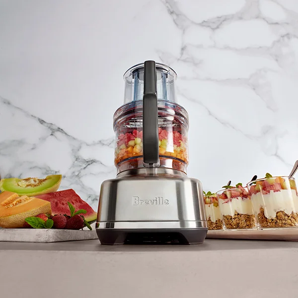 The Breville the Paradice 16 food processor sitting next to plates of fruit and fruit parfait while chopped up fruit sits in the bowl