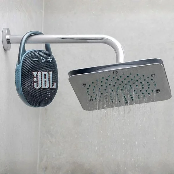 A blue JBL Clip 5 speaker clipped onto a shower head with the water on.