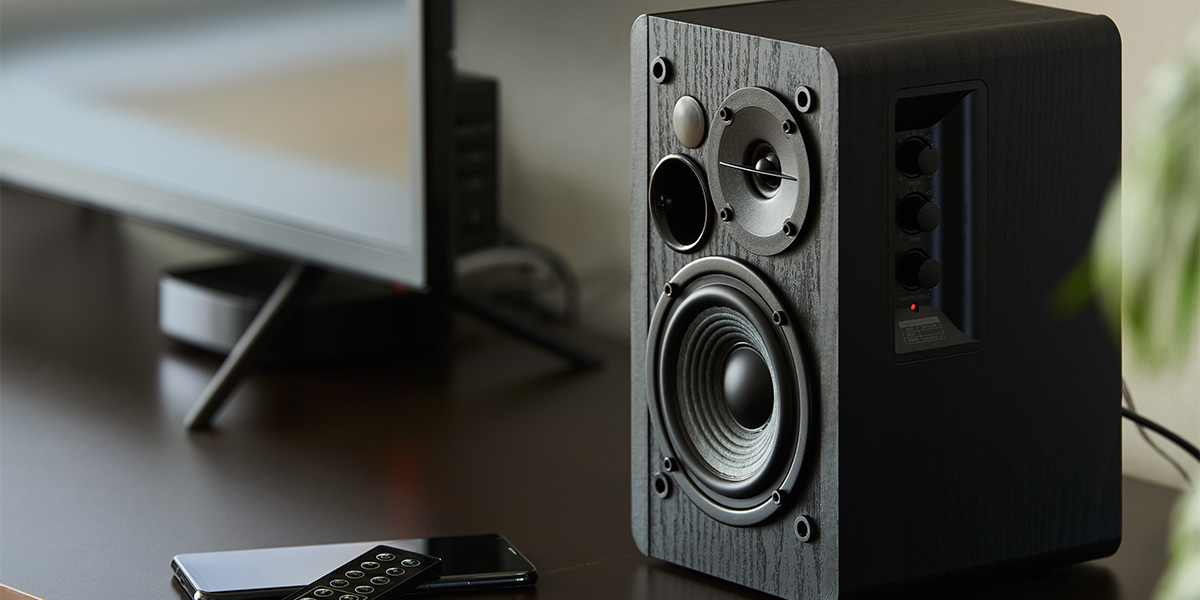 Close up of a bookshelf speaker sitting next to a TV